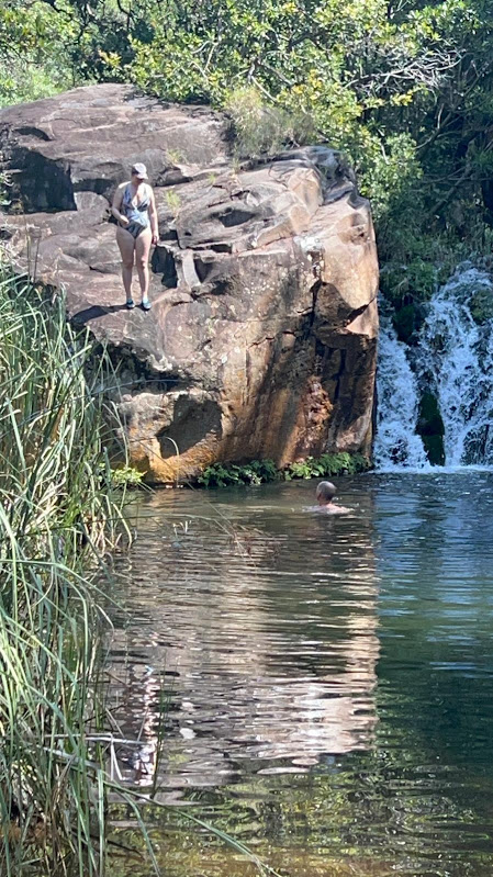 Erica on a rock beside a waterfall pool, with someone swimming below