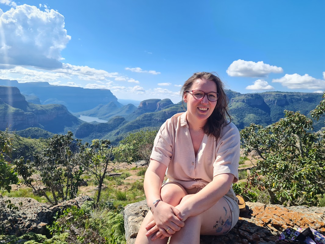 Erica sitting on a rock at a Blyde River Canyon viewpoint with the canyon behind her